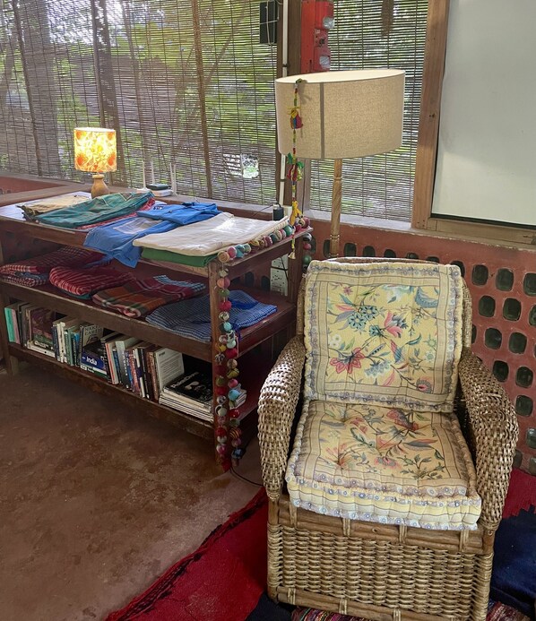 A room with a woven chair, a table with folded blankets, and a bookshelf filled with books.