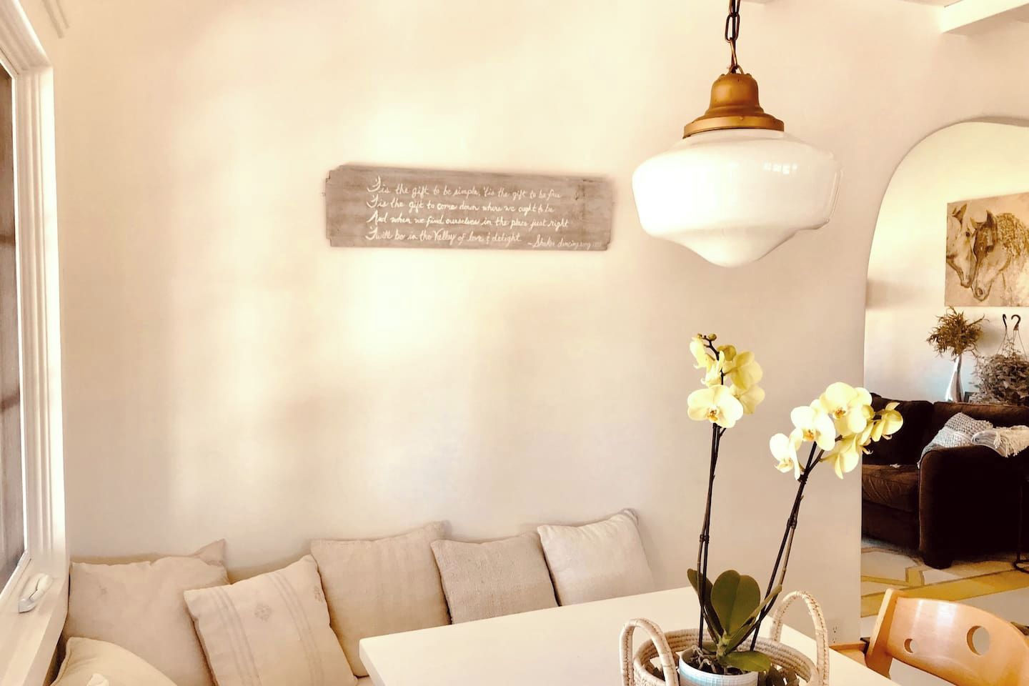 A living room with a white sofa, a table with a vase of flowers, and a wall-mounted sign.