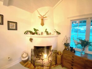 Une cheminée ornée d’une tête de cerf, entourée de plantes en pot et d’un banc en bois.