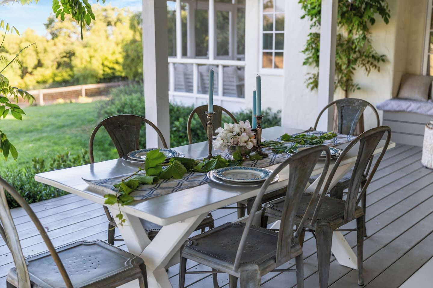 An outdoor dining area with a white table set for four, surrounded by metal chairs.