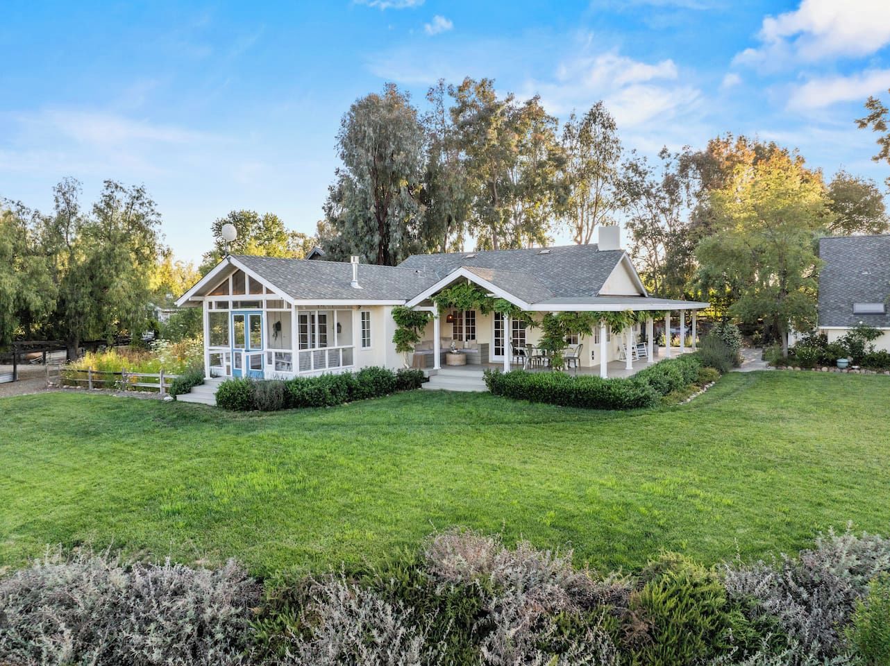 A two-story house with a covered porch, a well-maintained lawn, and mature trees in the background.