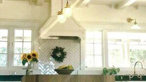 A kitchen with a herringbone tile backsplash, a hanging light fixture, a vase with flowers, and a fruit bowl. - Anavo Farm House ~ a storybook stay with Animals (Solvang)