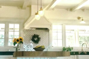 Une cuisine avec un dosseret de carreaux disposés en motif chevron, un luminaire suspendu, un vase rempli de fleurs et un panier de fruits.