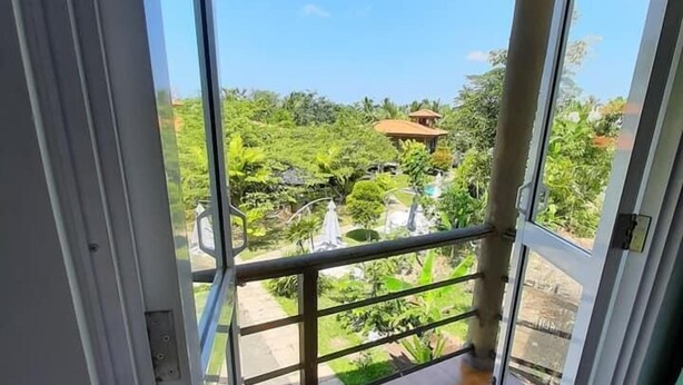 A balcony with a wooden floor and a metal railing, overlooking a lush garden and a distant building. - Mass Eco Cabana Yoga & Spa - Unawatuna (Unawatuna)