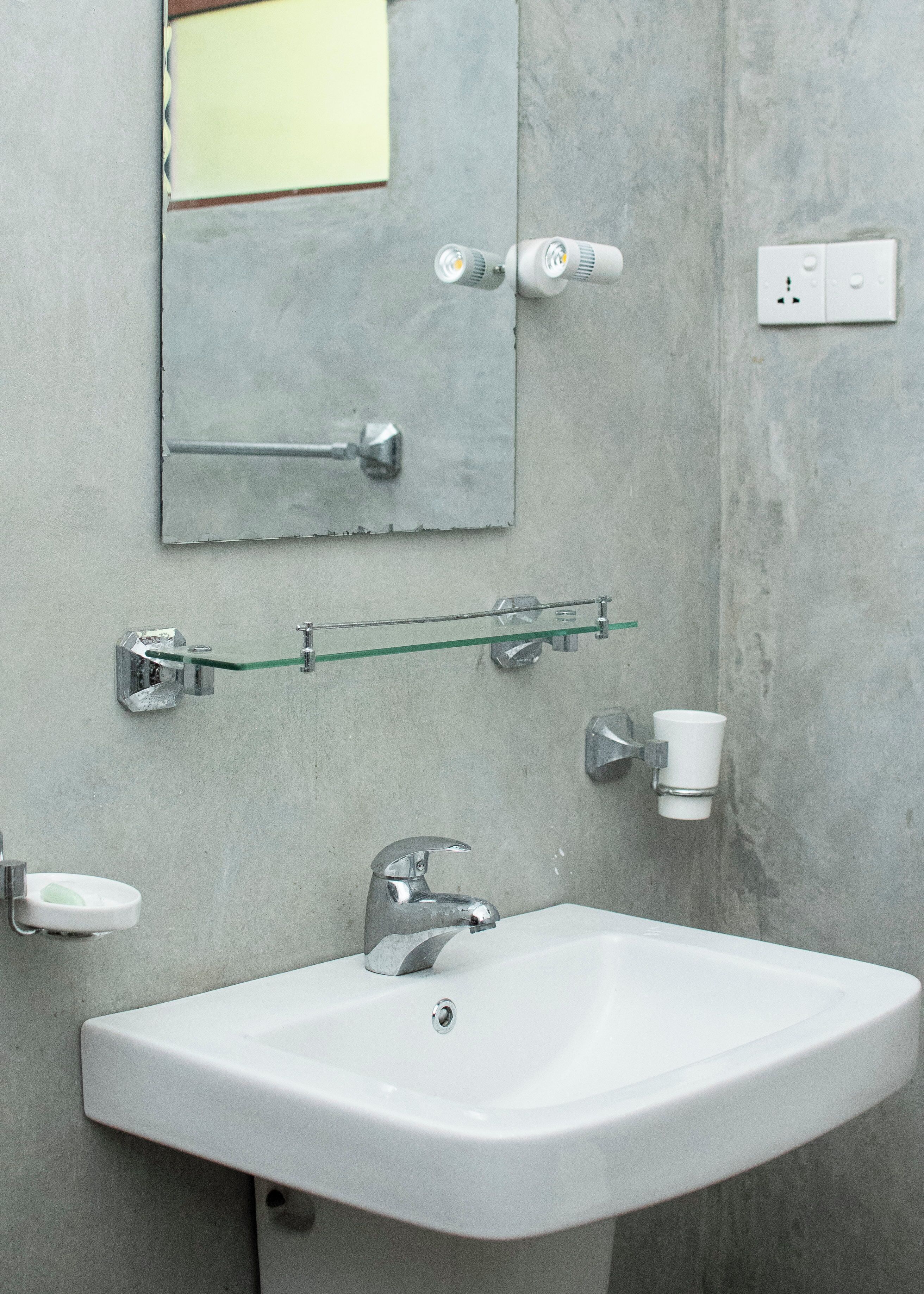 Une salle de bain avec un lavabo blanc, un miroir et une étagère en verre.