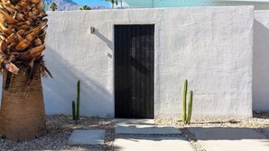 Een gebouw met witte muren, een zwarte deur, een palmboom en cactussen.