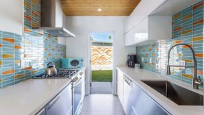Een moderne keuken met witte aanrechtbladen, een fornuis en een spoelbak. Er is een raam met uitzicht op een tuin.