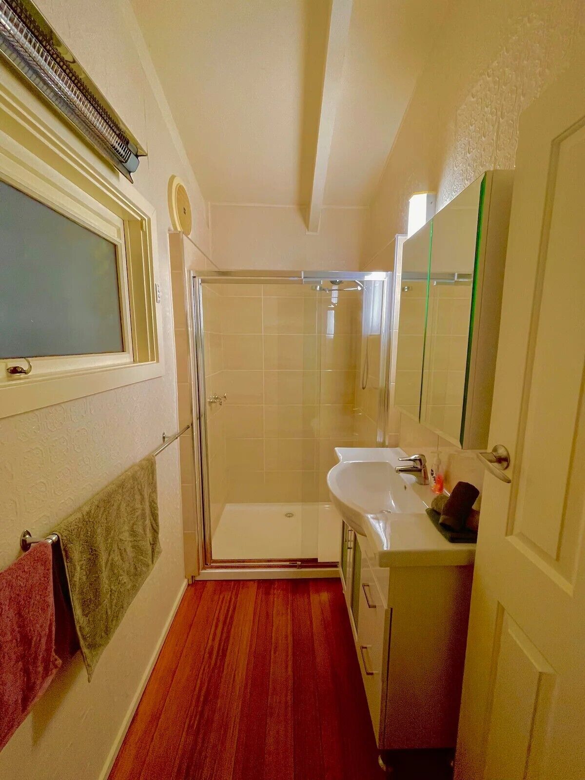 A compact bathroom with a glass-enclosed shower, a sink with a mirror, and a window with a frosted glass panel.
