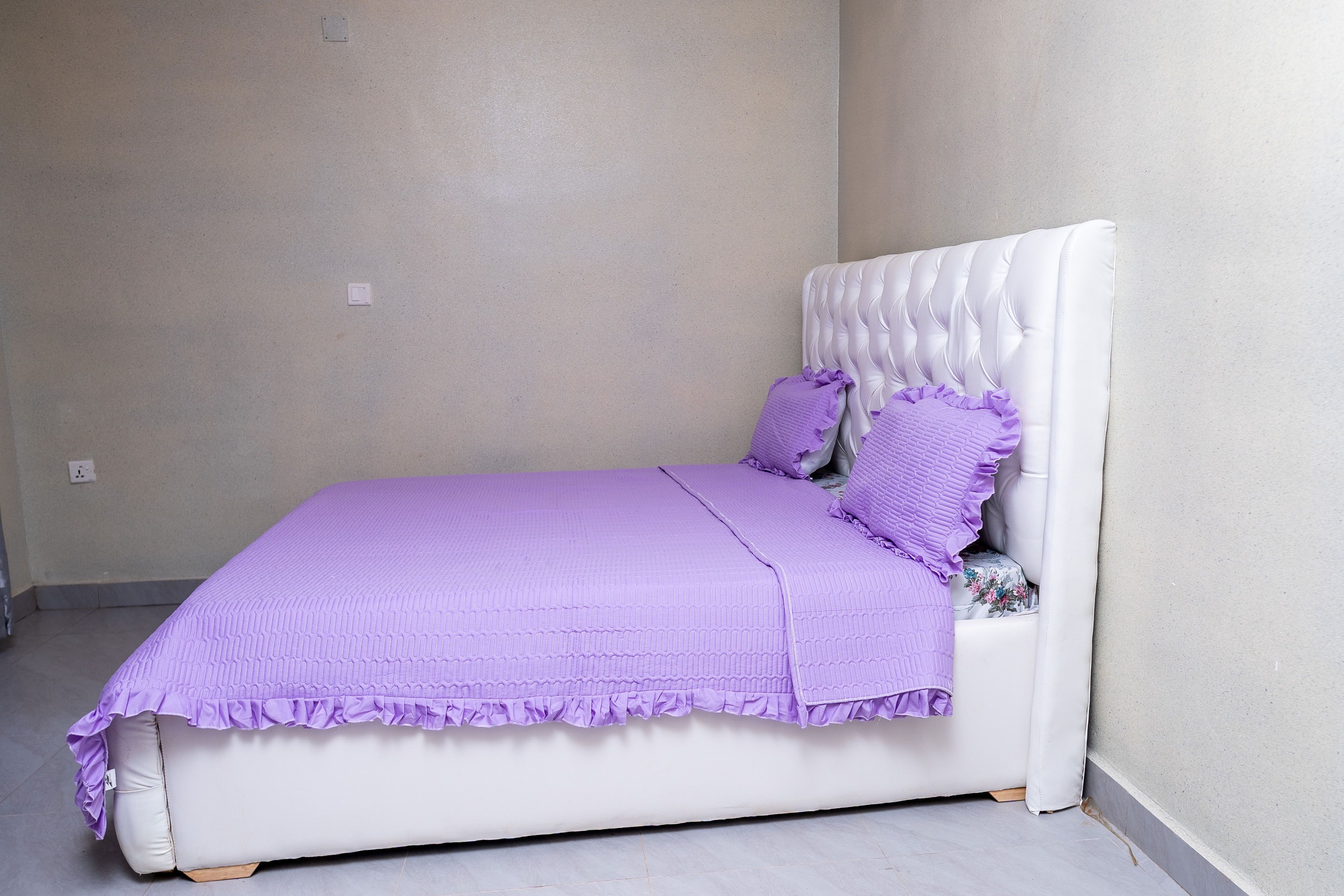 A neatly made bed with a white headboard and purple bedding.