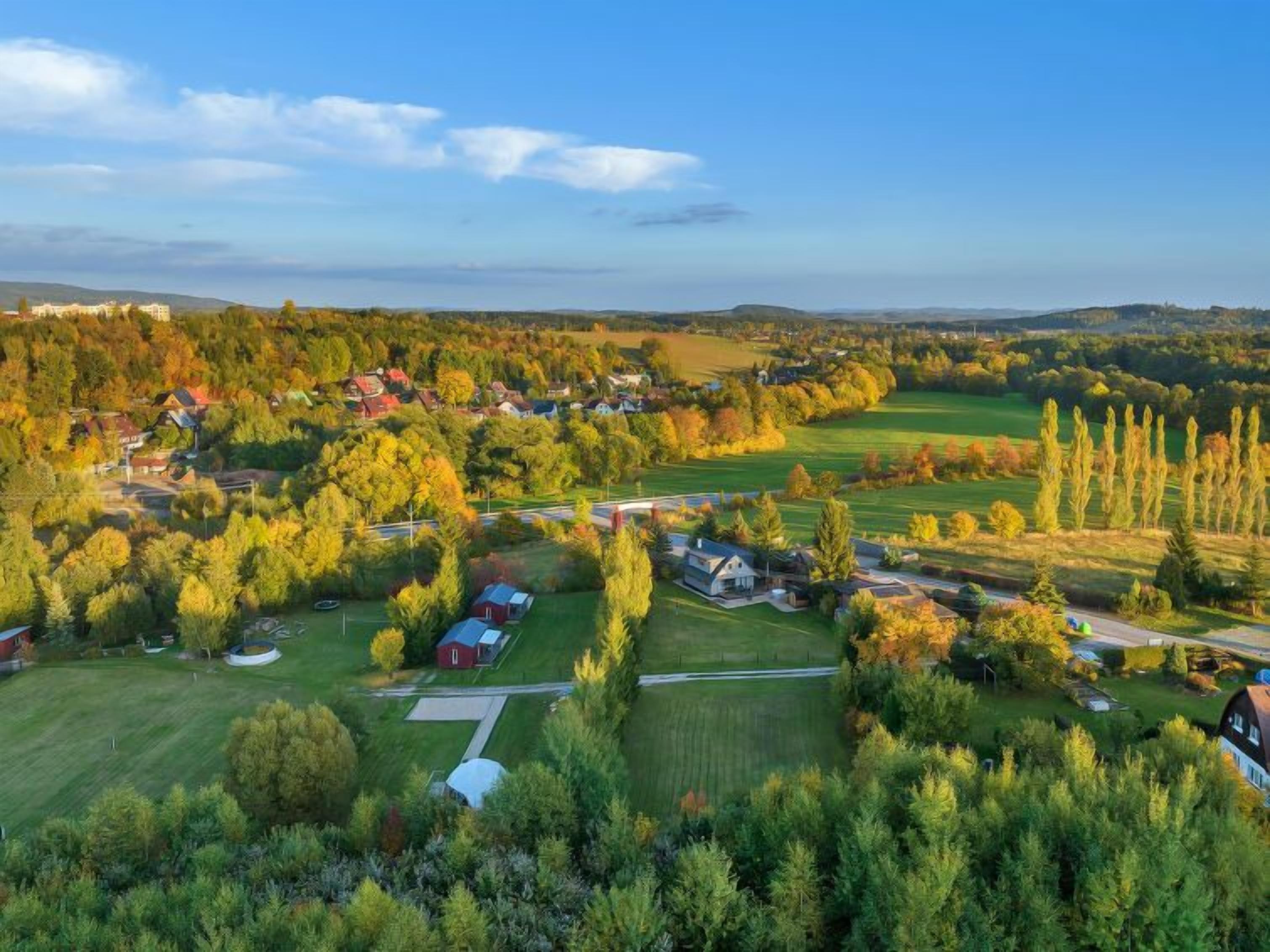 An aerial view of a residential area with houses, green fields, and trees.