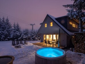 Una casa con un jacuzzi en el patio trasero, rodeada de árboles cubiertos de nieve.