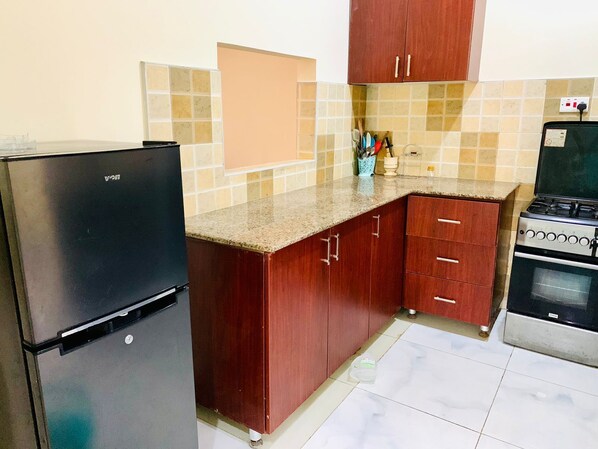 A kitchen with a black refrigerator, wooden cabinets, a granite countertop, and a stove.