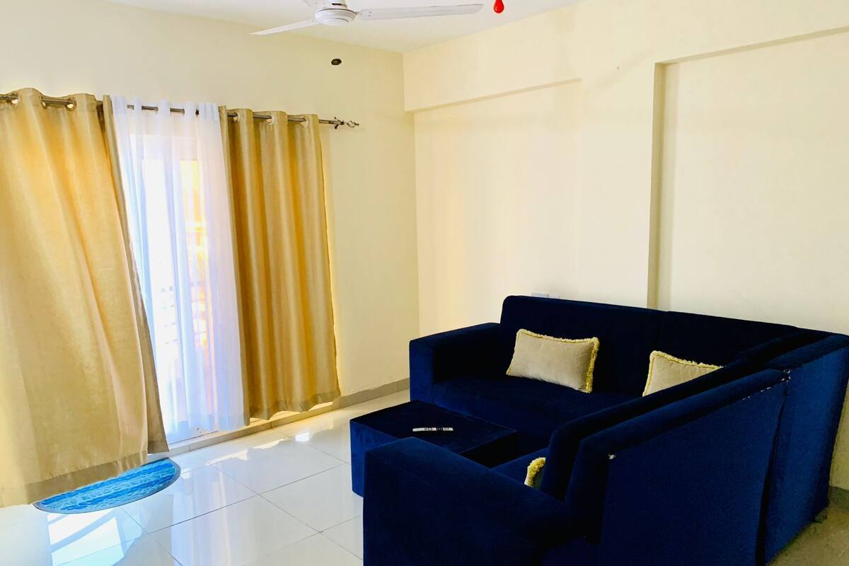 Una habitación con un sofá azul oscuro, suelo blanco y cortinas color beige.