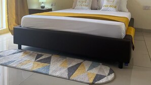 A neatly made bed with a yellow and white bedspread, two pillows with text, a framed picture on the wall, and a patterned rug on the floor. - Lux Suites Palm Terraces Apartments  (Mombasa)