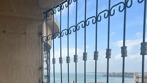 A balcony with a metal railing overlooking a coastal area with buildings and greenery. - Lux Suites Palm Terraces Apartments  (Mombasa)