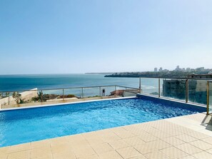 A rooftop swimming pool with a clear view of the ocean and city skyline.