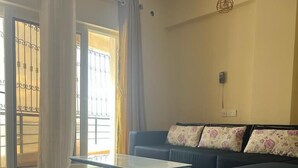 A modern living room with a glass coffee table, a dark sofa with floral cushions, and a grey rug. - Lux Suites Palm Terraces Apartments  (Mombasa)