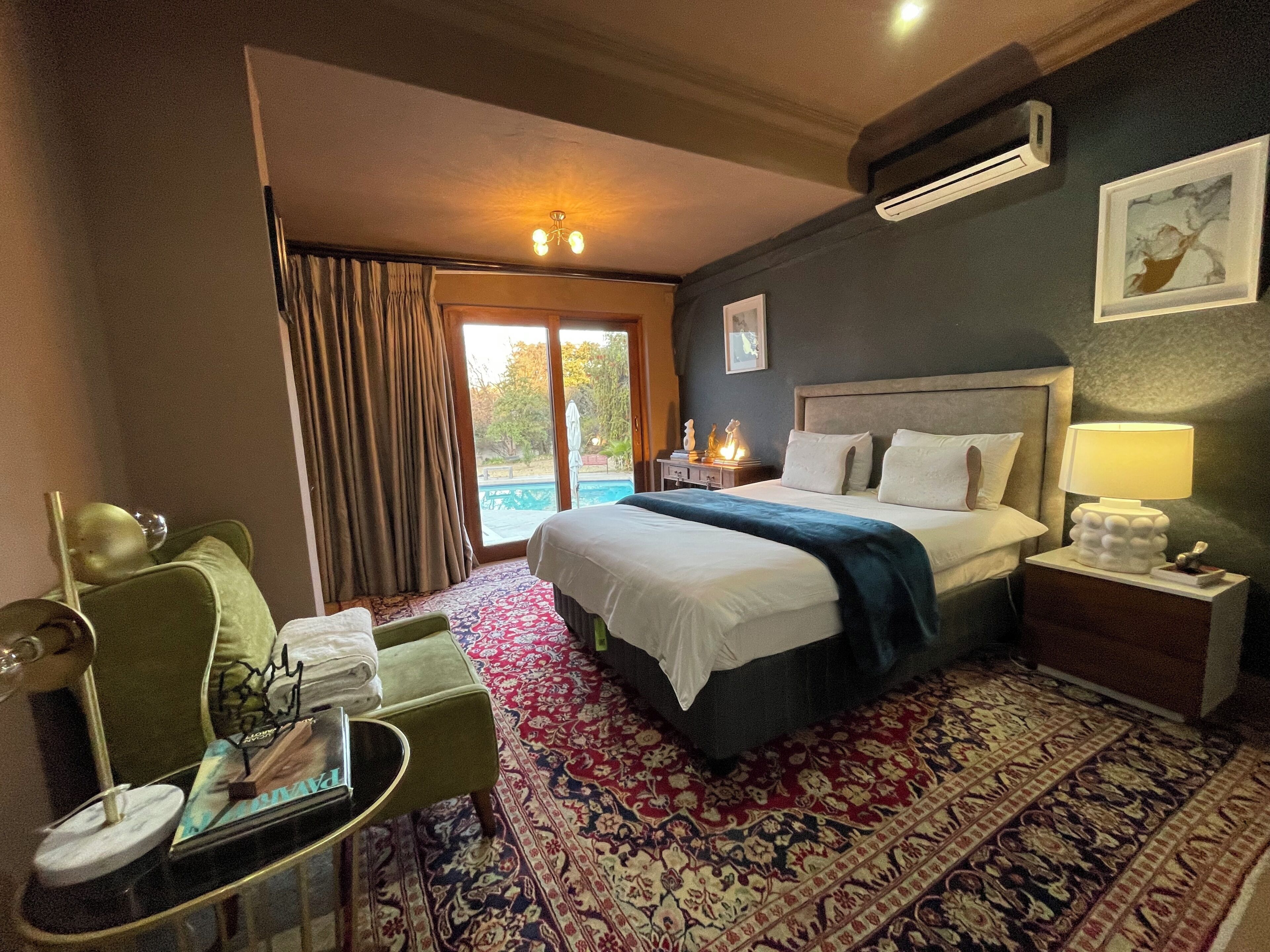 A hotel room with a bed, a desk, a chair, a table with a lamp, and a view of the outdoors.
