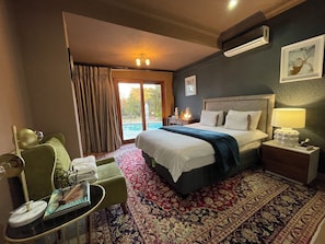 A hotel room with a bed, a desk, a chair, a table with a lamp, and a view of the outdoors.