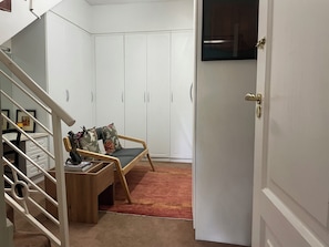 A hallway with a wooden chair, a small table, and a red carpet. There are white cabinets and a door with a brass handle.