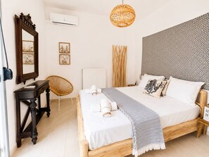 A bedroom with a wooden bed, a bedside table, a chair, a hanging light fixture, and a patterned wall. - Urban Red (Rethymno)