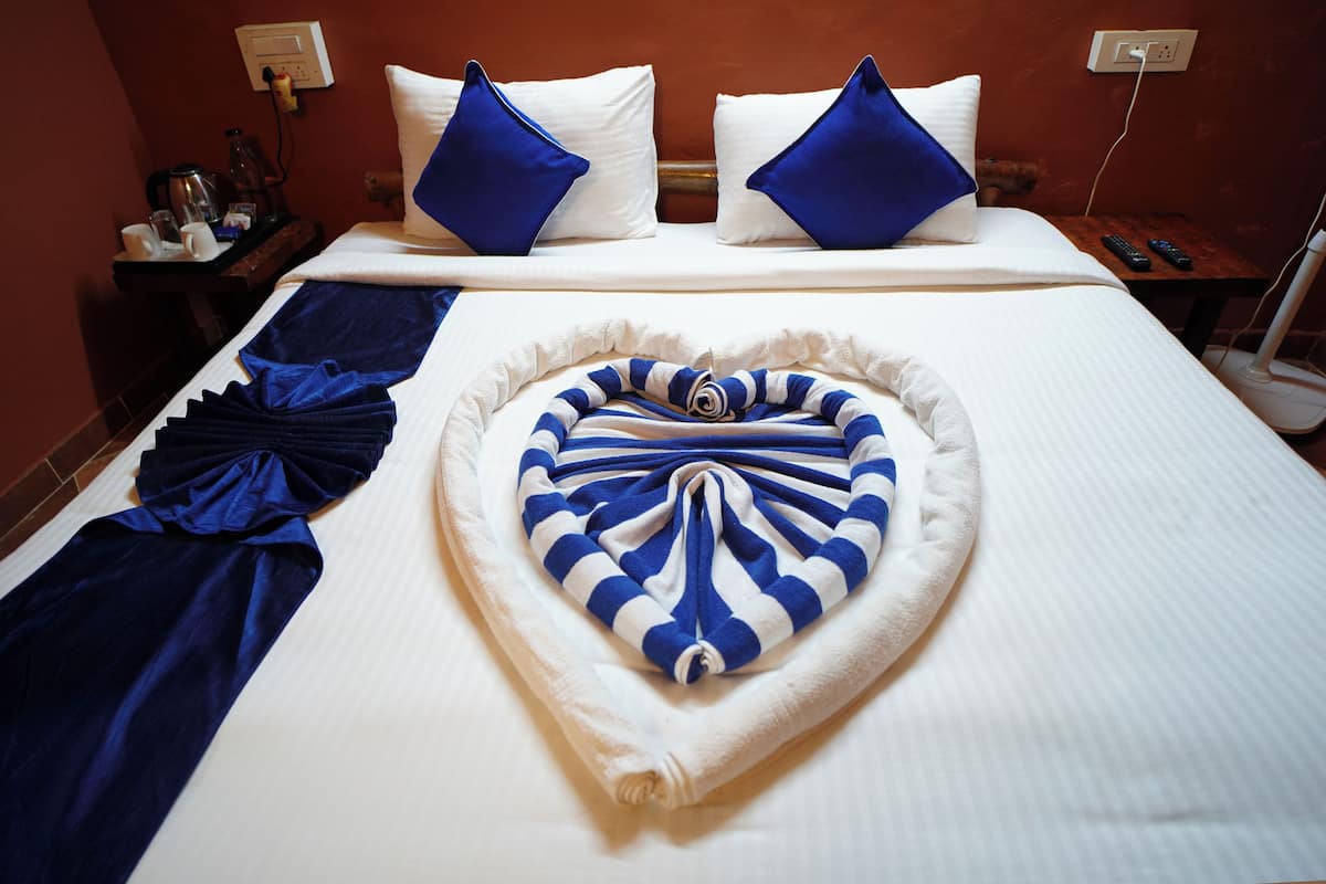 A hotel room with a neatly made bed, a heart-shaped towel on the bed, and a blue and white striped towel.
