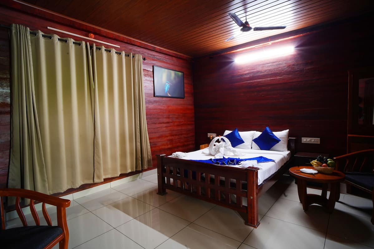 A hotel room with a wooden ceiling, a bed with blue and white bedding, a wooden chair, a small table with fruit, and a TV on the wall.