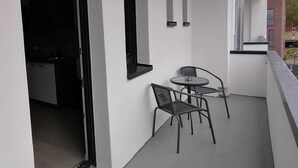 A balcony with a table and chairs, a door leading to a dark interior, and a window overlooking a building. - estrella24 LIVING ROOMS Venice (Herne)
