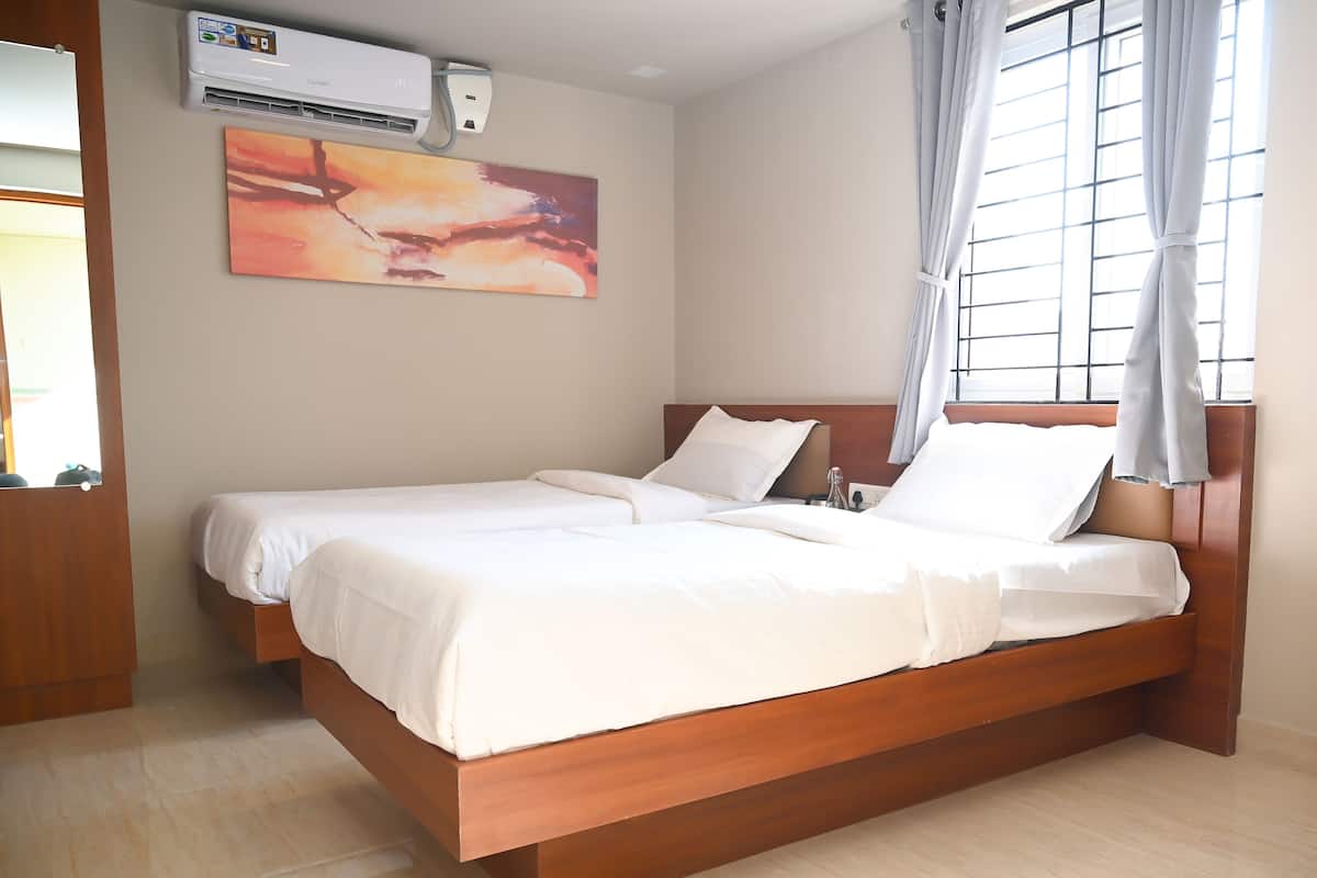 A bedroom with a wooden bed, a ceiling air conditioner, a window with curtains, and a painting on the wall.
