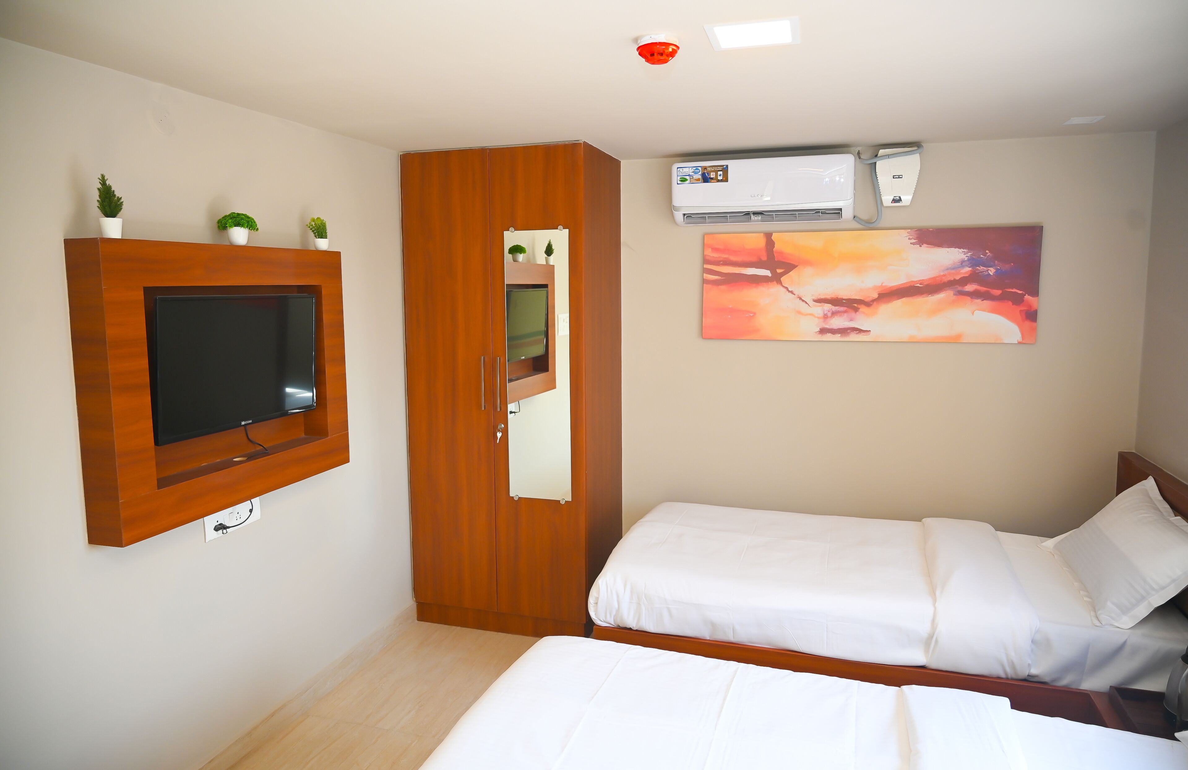 A bedroom with a TV mounted on the wall, a wardrobe, a bed, and an air conditioning unit.