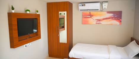 A bedroom with a TV mounted on the wall, a wardrobe, a bed, and an air conditioning unit.