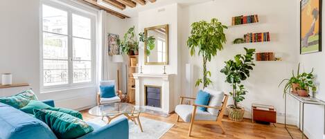 Una sala de estar moderna con chimenea, vigas de madera, un sofá, sillones y una estantería.
