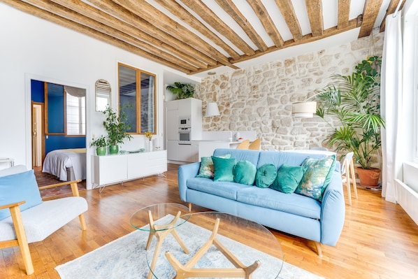 A living room with a blue sofa, wooden floor, stone wall, and a ceiling with exposed beams. - in the heart of Paris, premium, with beautiful plants and A/C (Paris)