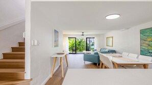 Een moderne woonkamer met een bank, eettafel en stoelen, een trap en een balkon met uitzicht op groen.