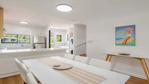 Een moderne keuken met een centraal eiland, een eethoek met tafel en stoelen, en een schilderij aan de muur.
