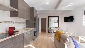 Una cucina moderna con elettrodomestici in acciaio inossidabile, un'area pranzo con divano e tavolo, e una TV montata a parete.