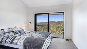 A bedroom with a large window, a bed with striped bedding, and a lamp. - Arana A Little Blue Mountains Luxury (WENTWORTH FALLS)