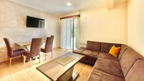 A modern living room with a brown sofa, a wooden coffee table, and a dining area with a table and chairs. - Apartments Boreta Becici (Becici)