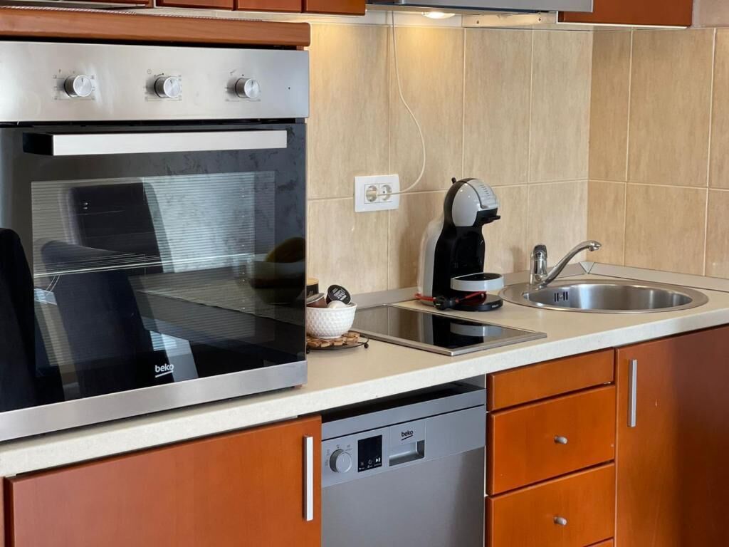 Een keuken met een inbouwoven, koffiezetapparaat, spoelbak en vaatwasser.