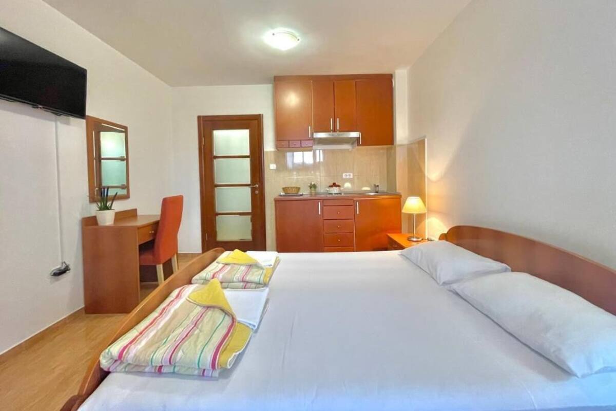 Ein Hotelzimmer mit Bett, Schreibtisch, Stuhl, einer Küchenzeile und einem Fernseher.