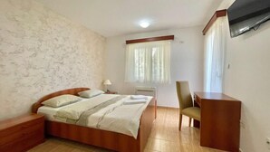 A bedroom with a wooden bed, a desk, a chair, a TV mounted on the wall, and a window with curtains. - Apartments Boreta Becici (Becici)