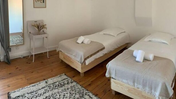 A bedroom with two single beds, a bedside table with a lamp, a mirror, and a patterned rug on a wooden floor. - « Maison Magnolia » Près de la Gare (Chasse-sur-Rhône)