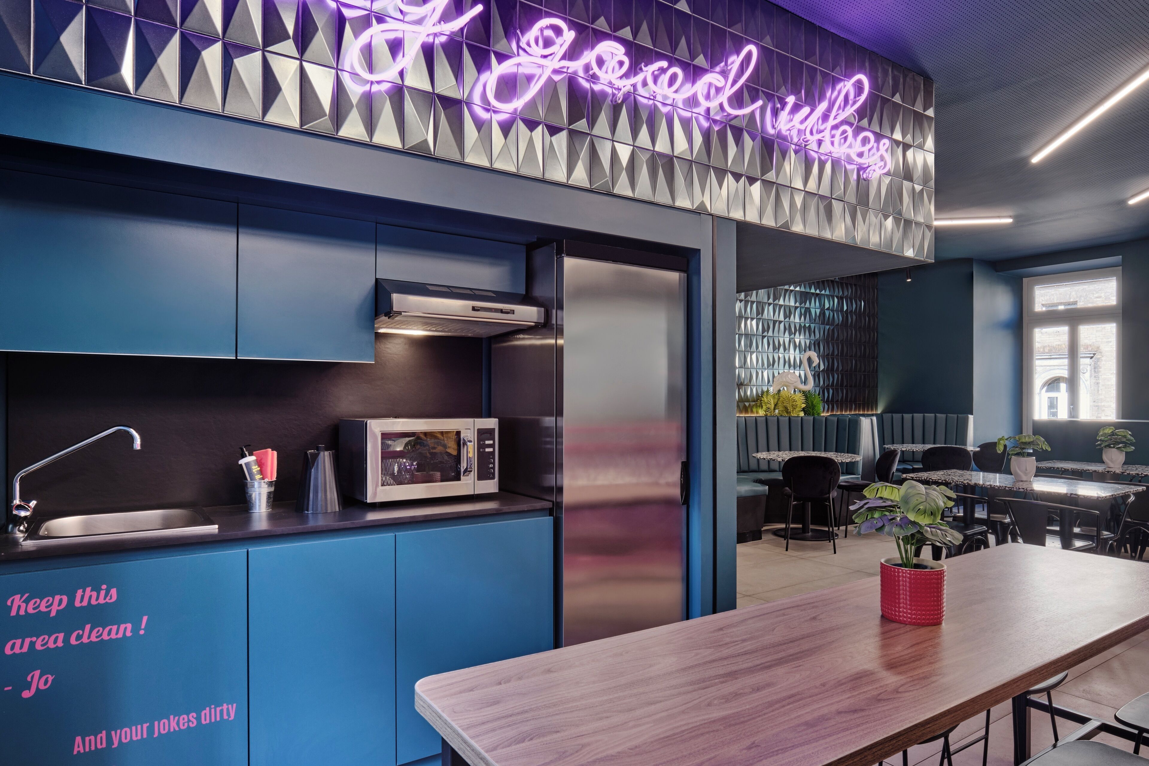 A modern kitchen with a neon sign, a sink, and a microwave.
