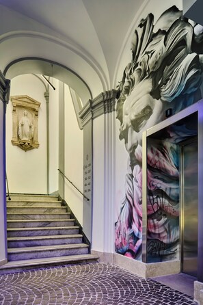 A staircase with a marble finish, a mural with floral and abstract designs, and a classical statue on the wall.