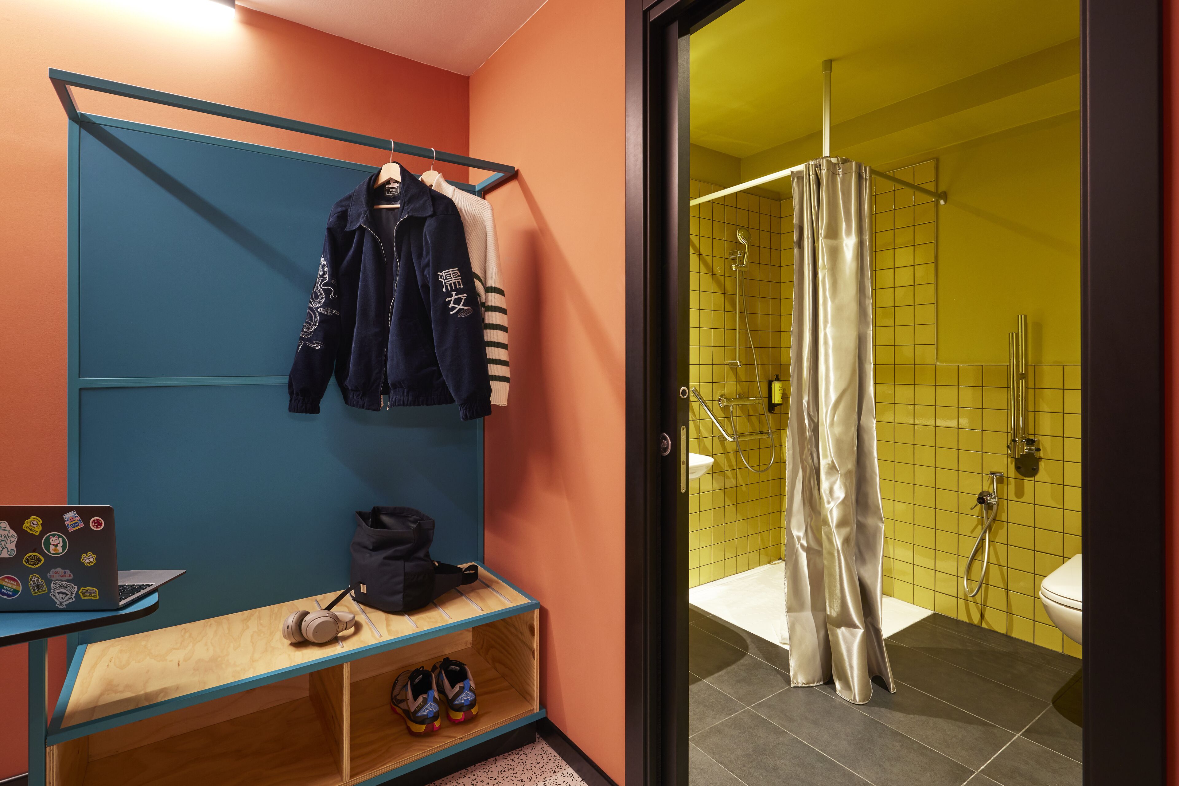 Een badkamer met een douche, een bank met schoenen en een rek met kleding.