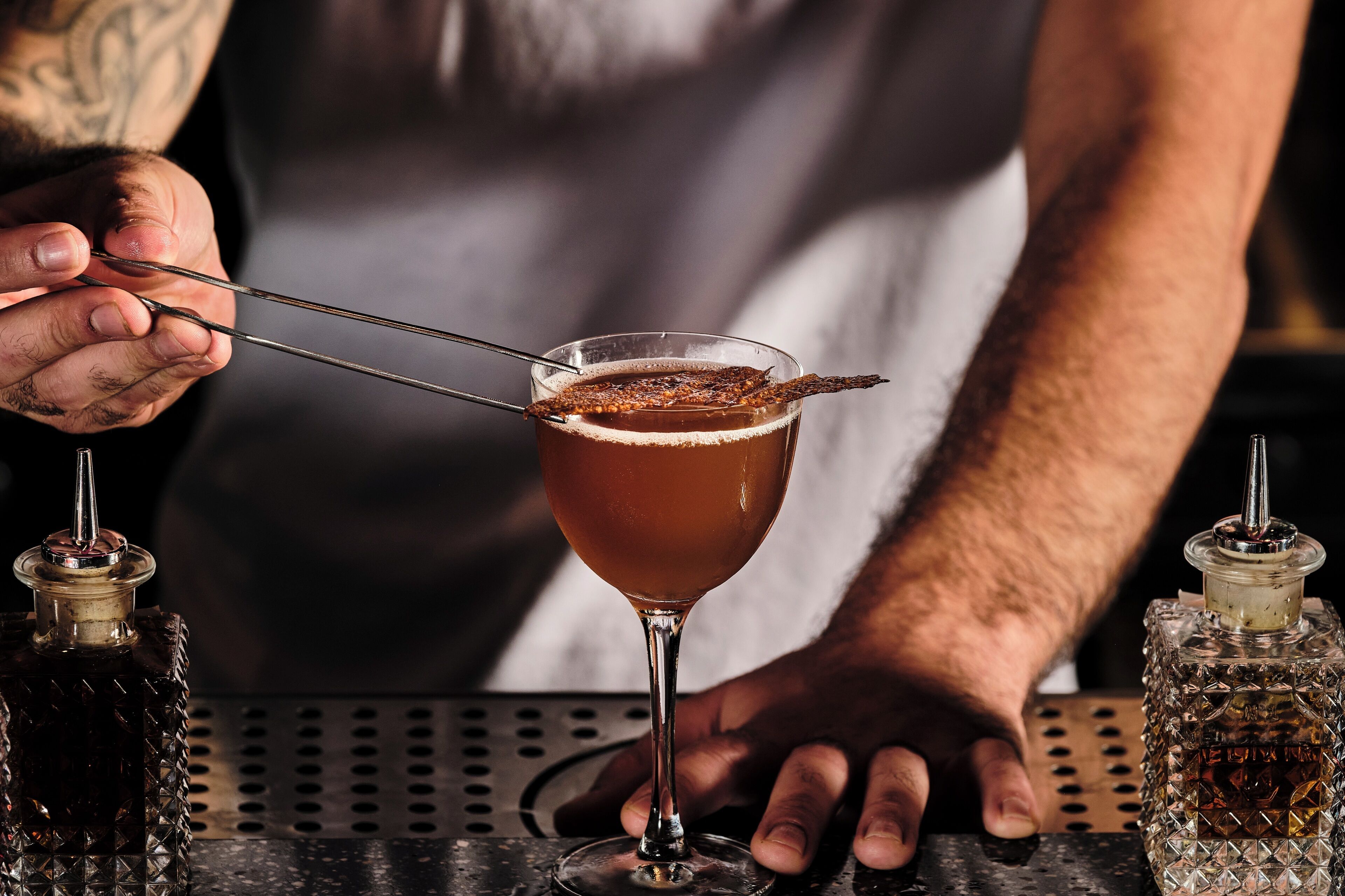 A bartender holding a cocktail shaker with a drink in a glass.