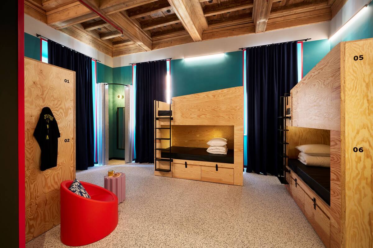 Ein Zimmer mit Etagenbetten, einem roten Sessel, einem Holzschrank und einem kleinen Tisch.