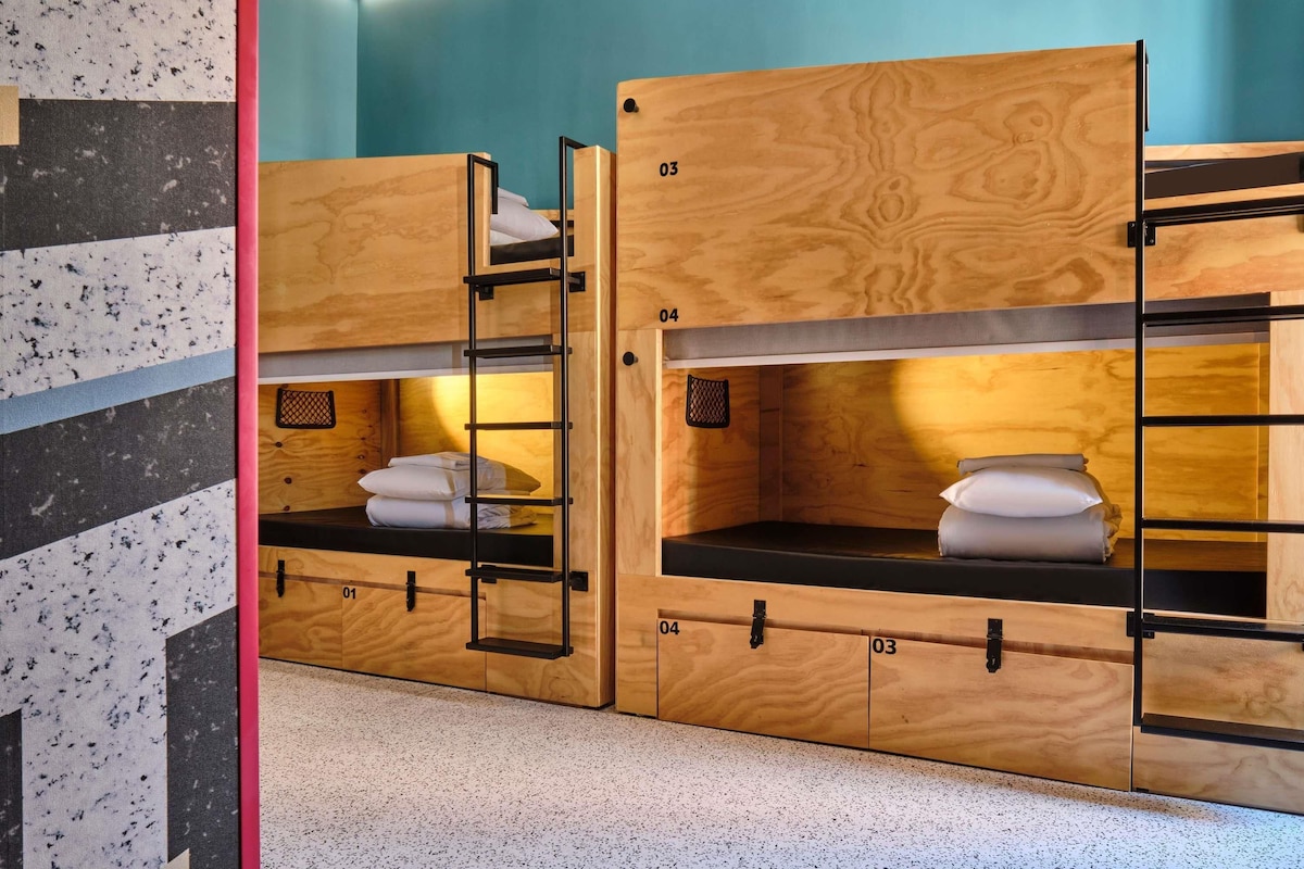 A bunk bed room with wooden bunk beds, numbered compartments, and a small shelf with pillows.
