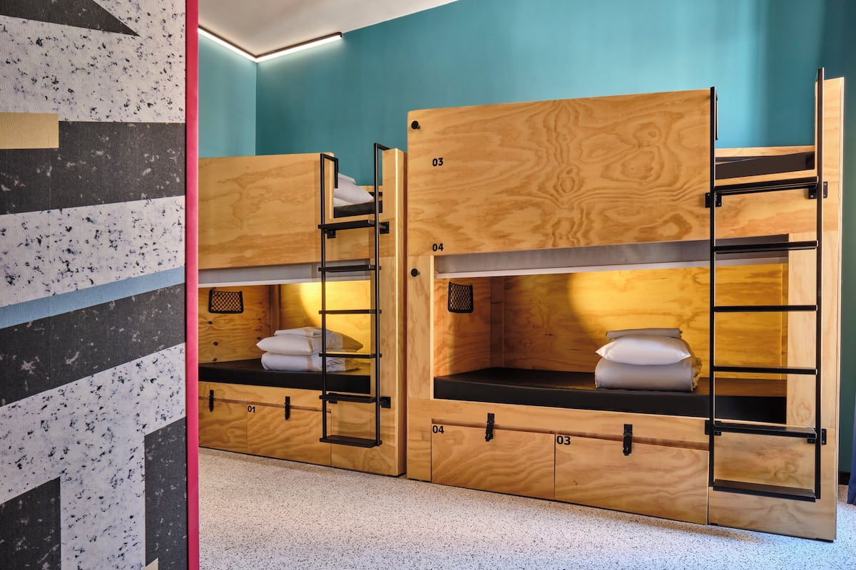 Ein Bunkebett-Set mit integrierten Stauraumfächern, nummeriert von 01 bis 04, in einem Zimmer mit türkisfarbenen Wänden und einem punktierten Boden.