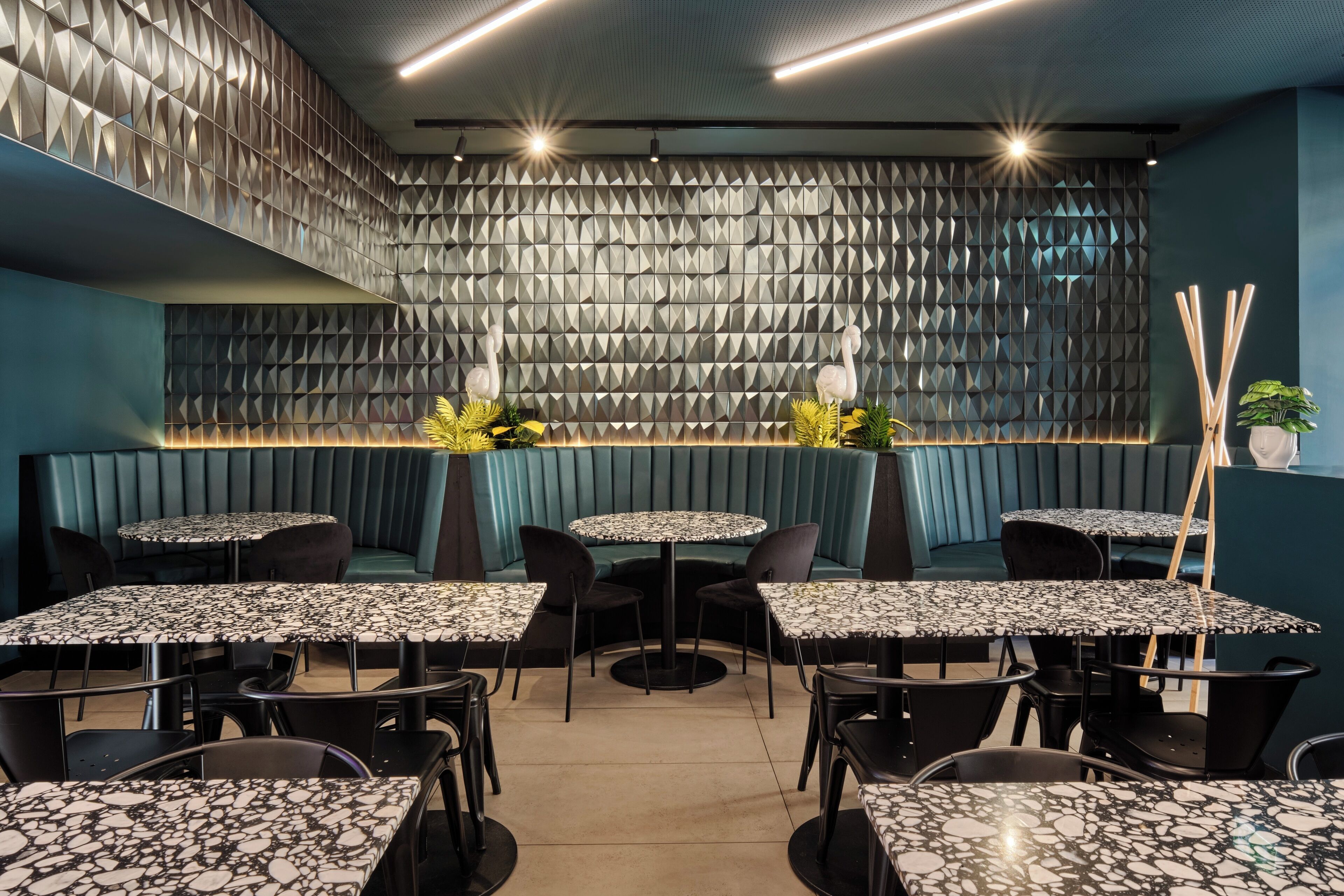 Ein modernes Restaurantambiente mit geometrischen Wandverkleidungen, blaugrünen Sitzbänken und Tischen mit Marmorplatten.